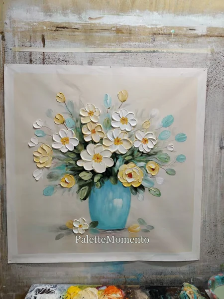White and yellow floral painting in a turquoise vase above the studio palette