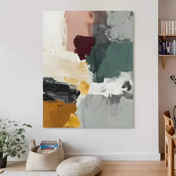 Sage green, gray, and maroon abstract painting in heavy impasto, hung on a white wall above a linen pouf and a woven basket of books in a cozy reading corner with wall-mounted shelves