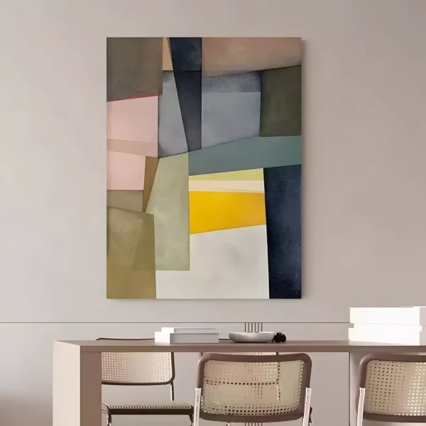 Geometric color-block canvas in soft pink, olive sage, slate gray, and deep navy panels with one yellow wedge near the center, hung on a warm greige wall above a taupe dining table with cane-back chairs