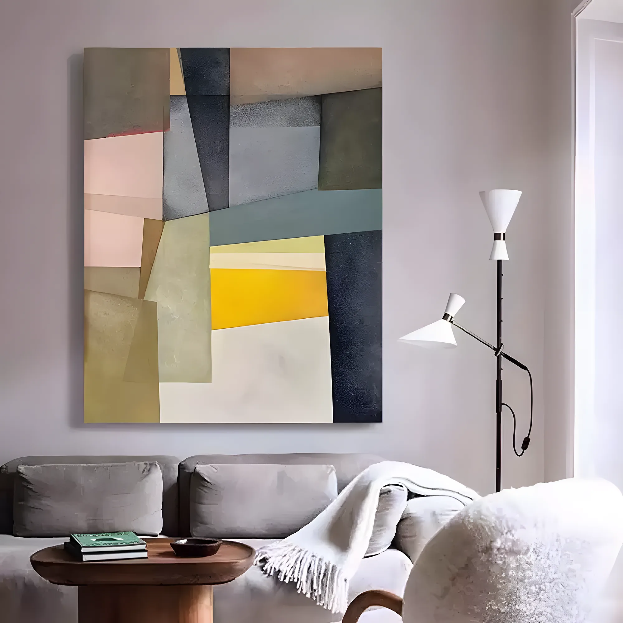 Color-block abstract painting with angled pink, khaki green, charcoal, and yellow planes stacked in a tall grid, mounted on a pale gray wall behind a gray sofa