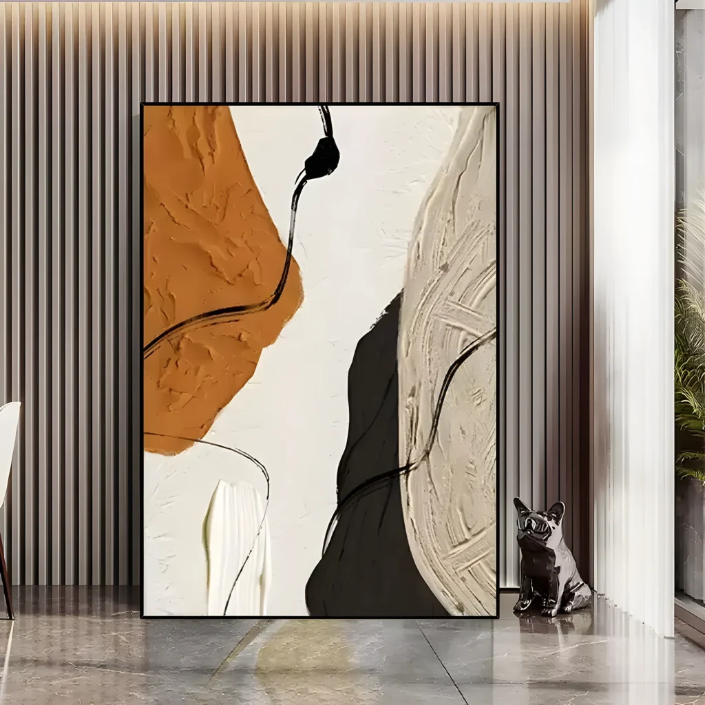 Tall black-framed wabi-sabi canvas in burnt orange, cream, taupe, and charcoal thick paint, standing against a gray slat-panel wall in an entryway with a polished marble floor and a ceramic bulldog figurine