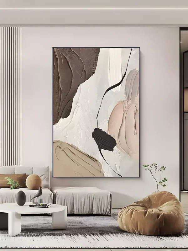 Beige and peach wabi-sabi painting with a dark chocolate impasto sweep, blush ridges, and a thin black line, hung in a slim navy frame above a light gray modular sofa, white round coffee table, and tan bean bag