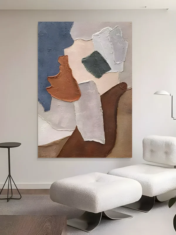 Blue and rust torn-paper wabi-sabi painting with slate blue, terracotta, ivory, and a small pine green patch in heavy impasto, on a white wall behind two white boucle ottomans and a black tripod side table