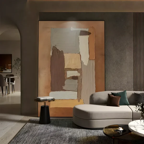 Brown and tan torn-paper wabi-sabi painting with gray, cream, and yellow ochre blocks on a caramel ground, framed in thin black on a charcoal wall behind a light gray curved sofa with green and brown pillows