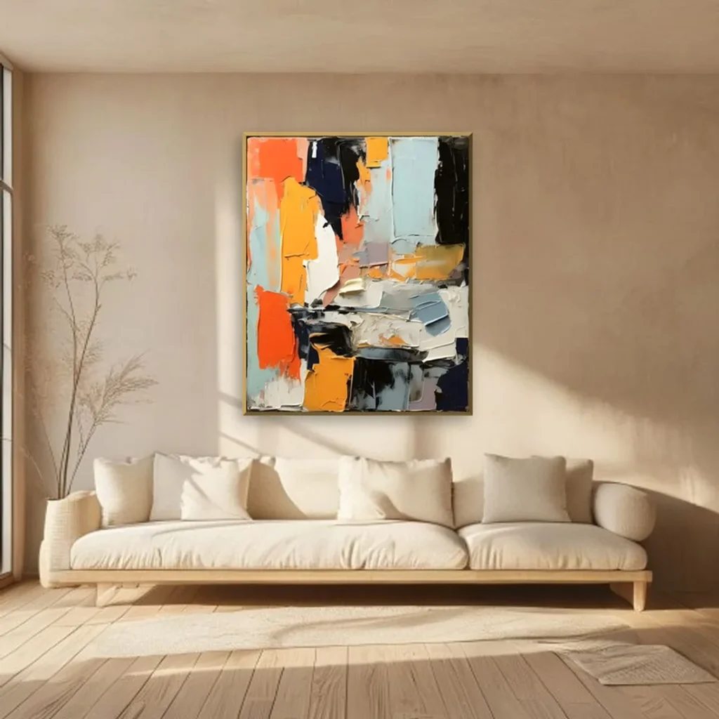 Maximalist wall art built from thick paint patches of orange, golden yellow, black, and powder blue, framed in gold above a long cream sofa in a beige plaster living room with dried stems nearby