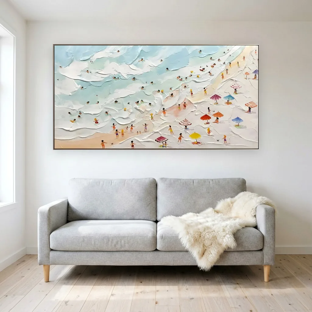 Aerial summer beach canvas painting with tiny swimmers and colorful umbrellas along pale sand and raised white surf, hung over a light gray sofa draped with a sheepskin throw in a white-walled Scandinavian living room.