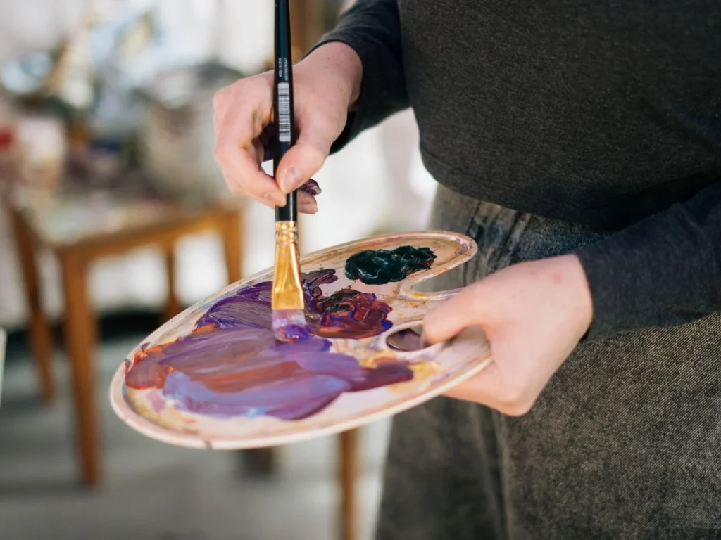 Artist mixing oil paint on a wooden palette before painting a made-to-order canvas