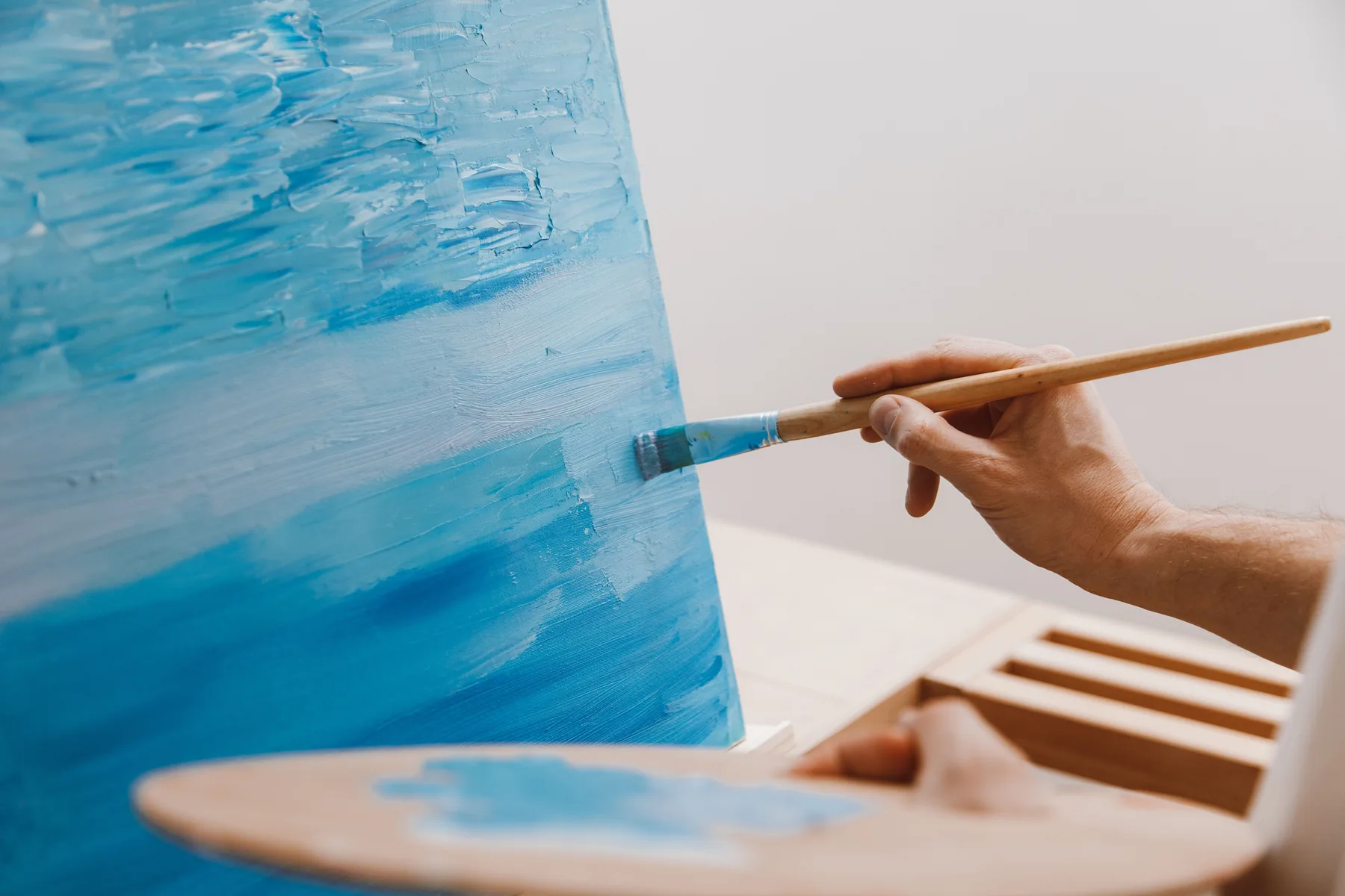 Illustrative stock photograph of an unrelated painter applying blue paint to a canvas with a brush.