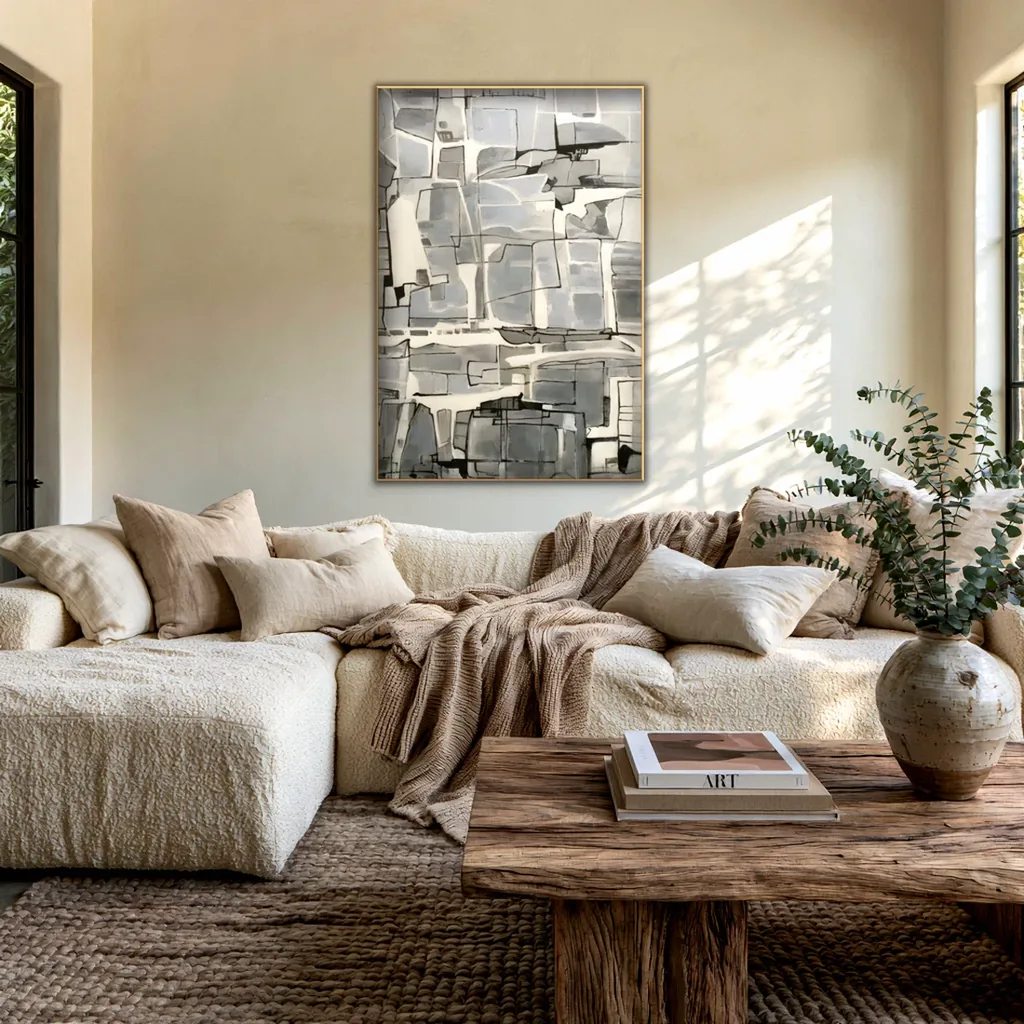 Gray and ivory geometric abstract in a thin gold frame on a warm cream plaster wall above a cream boucle sectional with linen pillows, a taupe knit throw and a reclaimed wood coffee table