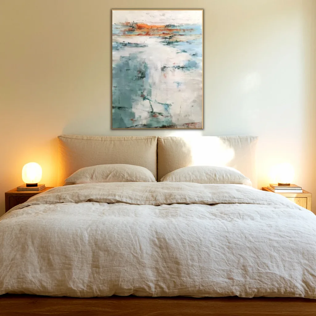 Sea green and white abstract painting with an orange band above a beige linen headboard and oatmeal bedding, between two glowing globe lamps