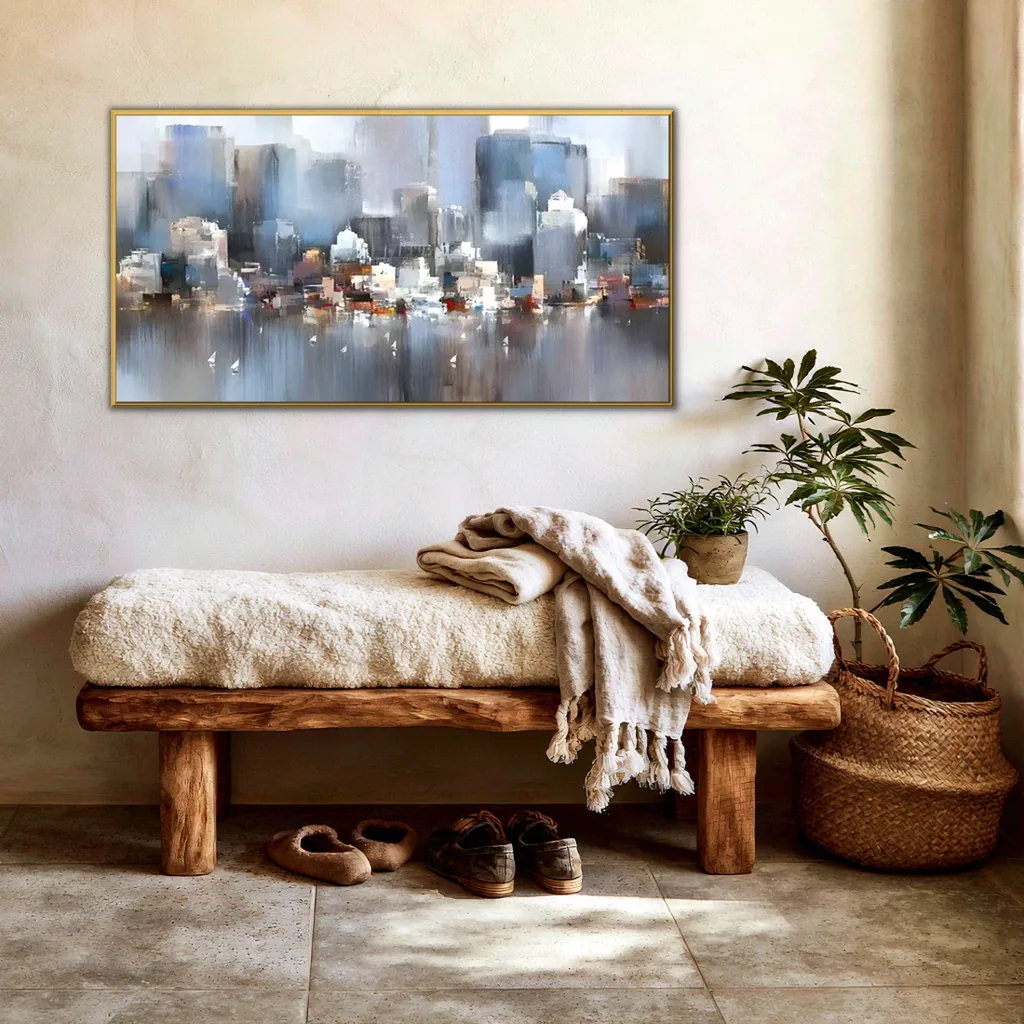 Misty blue and gray skyline painting in a gold frame on a cream plaster wall of an entryway, above a rustic wood bench with a sheepskin and a fringed throw, a potted plant in a woven basket and shoes underneath