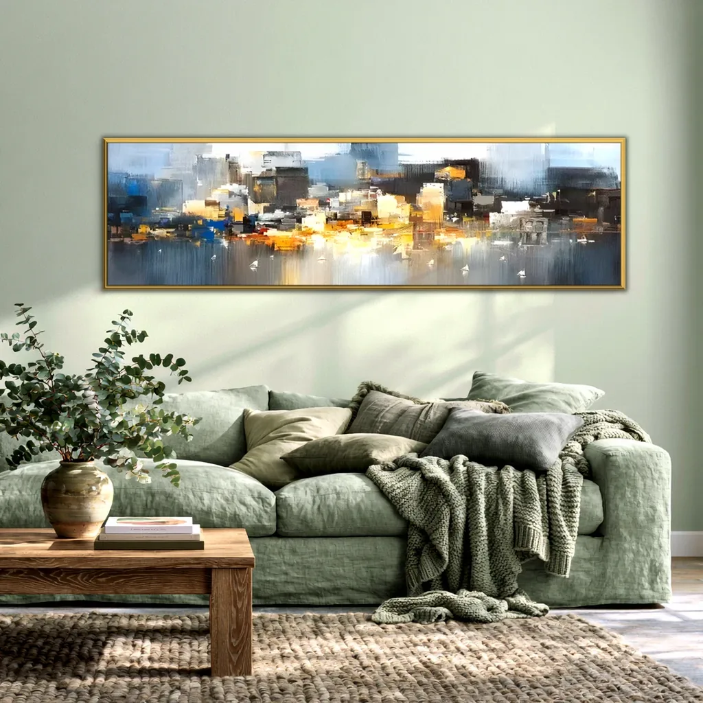 Panoramic gold and gray city skyline painting in a thin gold frame on a pale sage wall, above a sage linen sofa with a knit throw, a wood coffee table and eucalyptus in a stoneware vase